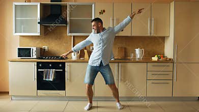 Handsome young funny man dancing in kitchen at home in the morning and have fun on holidays