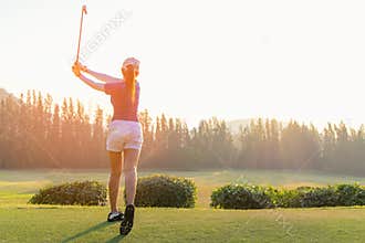 Asian woman golf player doing golf swing tee off on the green sunset evening time, she presumably does exercise