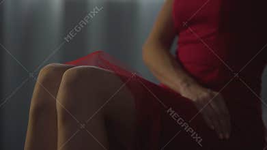 Appealing female in red dress elegantly crossing legs, smooth hairless skin