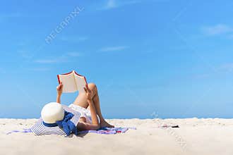 Woman laying and reading on the beach with blue sky in summer times.