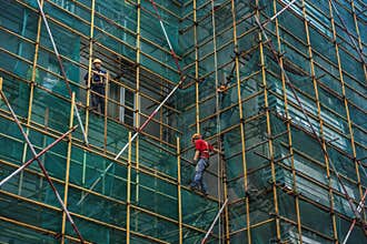 Construction workers working high up on dense scaffolding at building site, Nanjing China