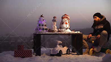 Snowman and snow xmas tree on winter landscape. Man in pilot glasses and hood on bike. Christmas and new year fun
