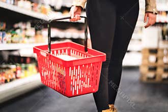 Woman holding shopping basket and walking in grocery store aisle