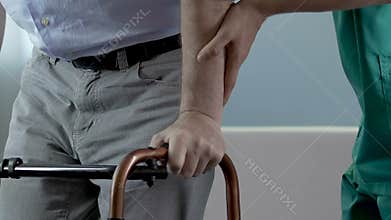 Man trying to make steps while holding on to walker, nurse supporting him by arm