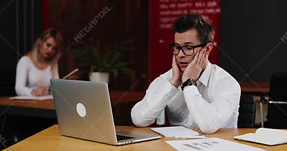 Stress at work. Young businessman looks very tired working in the office with laptop. Business, people, paperwork and