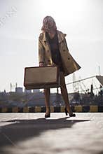 Attractive Young Blonde Woman in Trench with Vintage Suitcase on the Jacht Pier