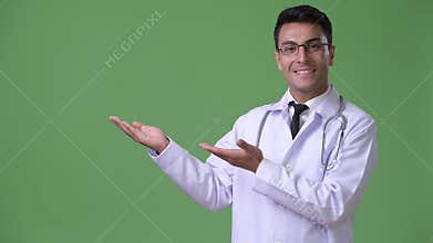 Young handsome Hispanic man doctor against green background