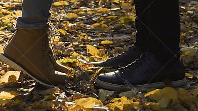 Close-up of shoes on leaf covered ground, girl reaching boyfriend to kiss, date