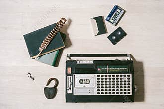 Old cassette tape recorder, key, lock, books and feather on wood