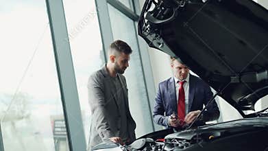 Professional automobile salesman is demonstrating customer car engine under motor hood, men are looking at auto parts