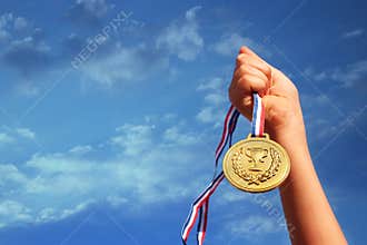 Child hand raised, holding gold medal against sky. education, success, achievement, award and victory concept.