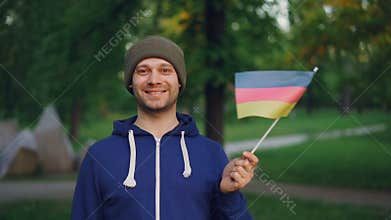 Slow motion portrait of male German sportsman handsome bearded man waving flag of Germany and smiling standing in city