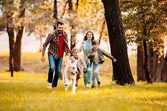 Happy family with two children running after a dog together