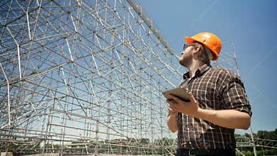 Young architect holding tablet and looking at metal installation on background, frowning and serious, planning and