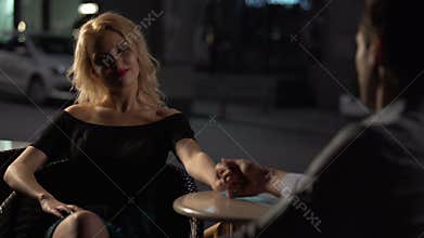 Blond woman sitting in cafe with boyfriend, man holding girlfriend's hand