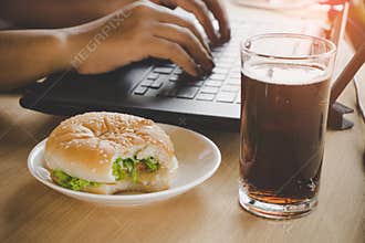 Business woman eating junk food burger and cold drink while working on computer laptop
