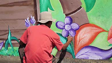 Mural painter draws flowers on concrete wall.