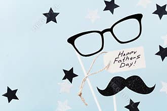 Happy Fathers Day background with greeting tag, glasses, funny moustache and star confetti on table top view. Flat lay style.