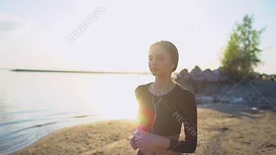 Young woman with smartwatch jogging by sea. Young sporty girl using smart watch on beach at sunset. Sun lens flare