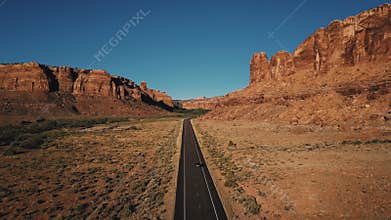 Aerial shot of car driving along straight American desert highway road among atmospheric rocky mountain canyon ridge.