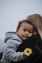 Young boy holding a flower carried by his mom