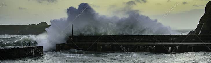 Stormy ocean waves crash over harbour wall