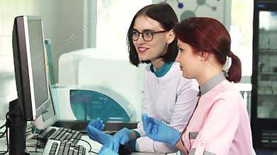 Two female lab workers operating analysing machines using computer