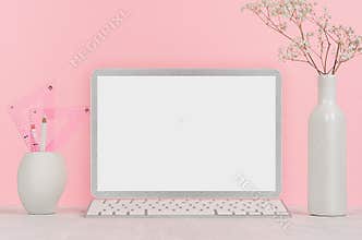 Elegant home workplace with stylish silver blank computer notebook and white stationery, flowers in vase on pink background.