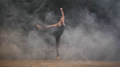 Young beautiful ballerina on smoke stage dancing modern ballet in the dark. Woman in black costume performs on scene