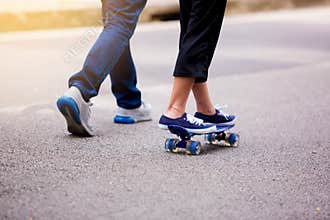 Young girl skateboarding with her dad running at park outdoor i