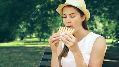 Hungry woman eating sandwich in park. Tourist having lunch in public park enjoying summer sunny day