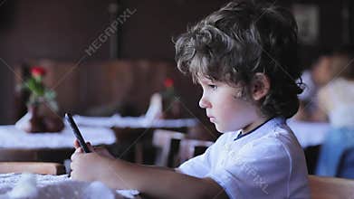 Little boy with mobile phone at cafe