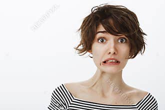 Studio shot of awkward cute european female student with stylish hairstyle, making mistake and blameful face, being
