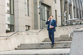 businessman with coffee to go talking by phone while walking by stairs