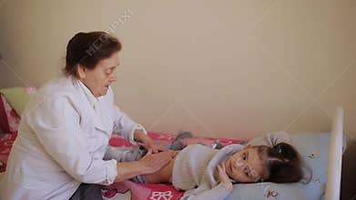 The elderly woman masseur doing massage of the abdomen to the little girl in the hospital.