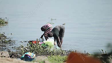 KENYA, KISUMU - MAY 20, 2017: Two african women staying on the shore of the lake and washing dishes together.