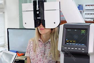 Young woman looking at refractometer eye test machine in ophthalmology