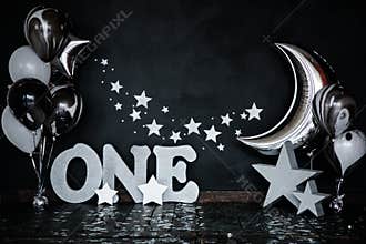 Smashed first birthday white cake with stars and one candle for little baby boy and decorations. Black background. Big silver lett