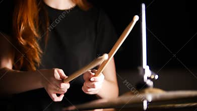 Red-haired girl plays music drums in a dark studio. Hands, drum sticks.