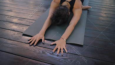Young woman in sportswear practicing yoga alone on wooden deck. Girl lying on fitness mat, doing body stretching with