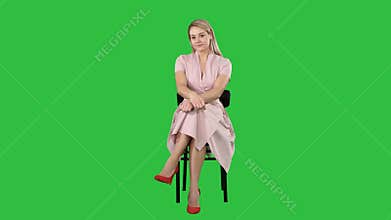 Beautiful young woman, girl, model blonde with long hair sitting on a chair and looking to camera on a Green Screen