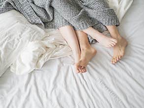 Close up of male and female feet on a bed - Loving couple under grey blanket in the bedroom - Concept of sensual and