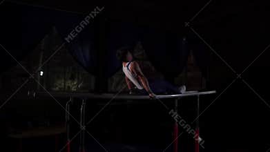Male gymnast acrobat performs handstand on parallel bars in a dark room in slow motion