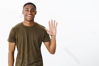 Friendly attractive nice african american male friend raising palm to wave smiling broadly saying hello, greeting