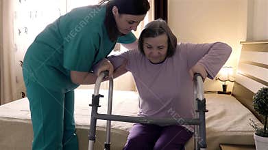 Caregiver helping senior woman getting up and walk with a walker