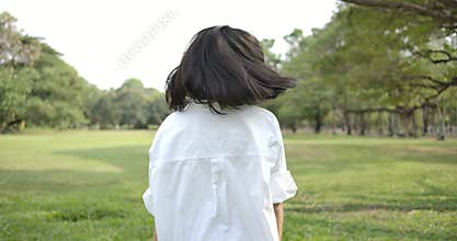 Close-up of a young attractive asian woman walking in a summer park at sunset, she goes and turn back to looks at the