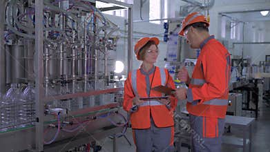 Heavy industry, happy female and male factory workers in helmets with computer tablet in hand near automatic belt line