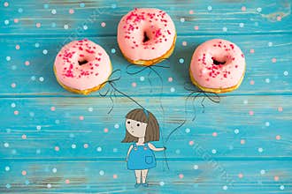 A conceptual photo of pink donuts on a blue wooden background. Hand-drawn cartoon girl holding donuts like inflatable balls