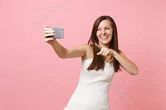Laughing bride woman in white wedding dress pointing index finger on camera doing taking selfie shot on mobile phone