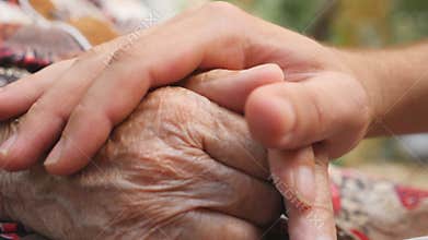 Close up of young male hand comforting an elderly arms of old woman outdoor. Grandson and grandmother spending time